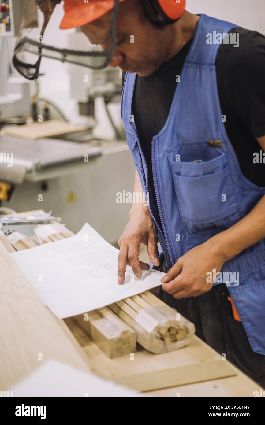 Il lavoratore falegname che legge il modello mentre lavora in magazzino Foto Stock