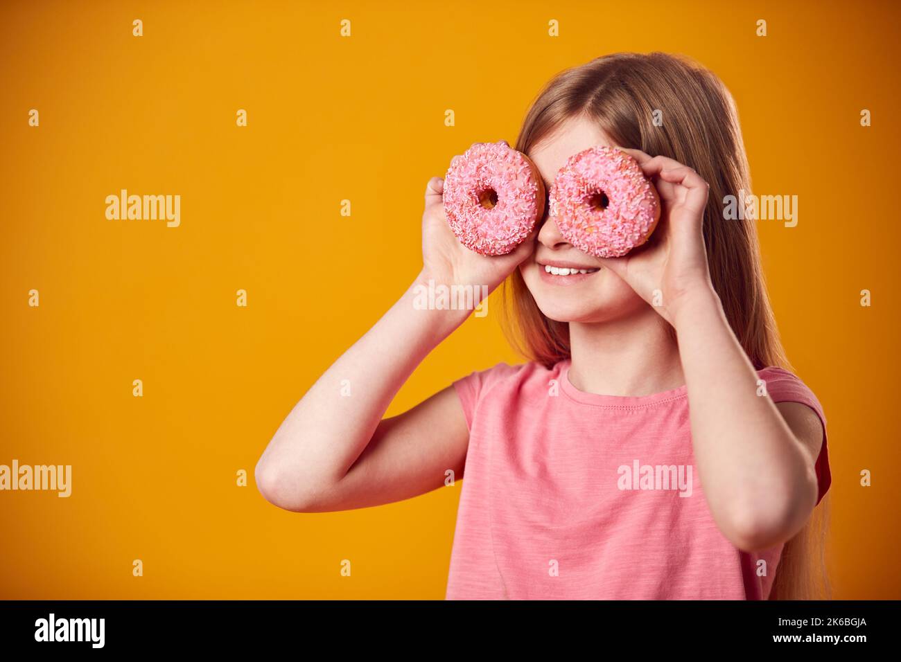 Studio Ritratto di ragazza che tiene due ciambelle davanti agli occhi contro sfondo giallo Foto Stock