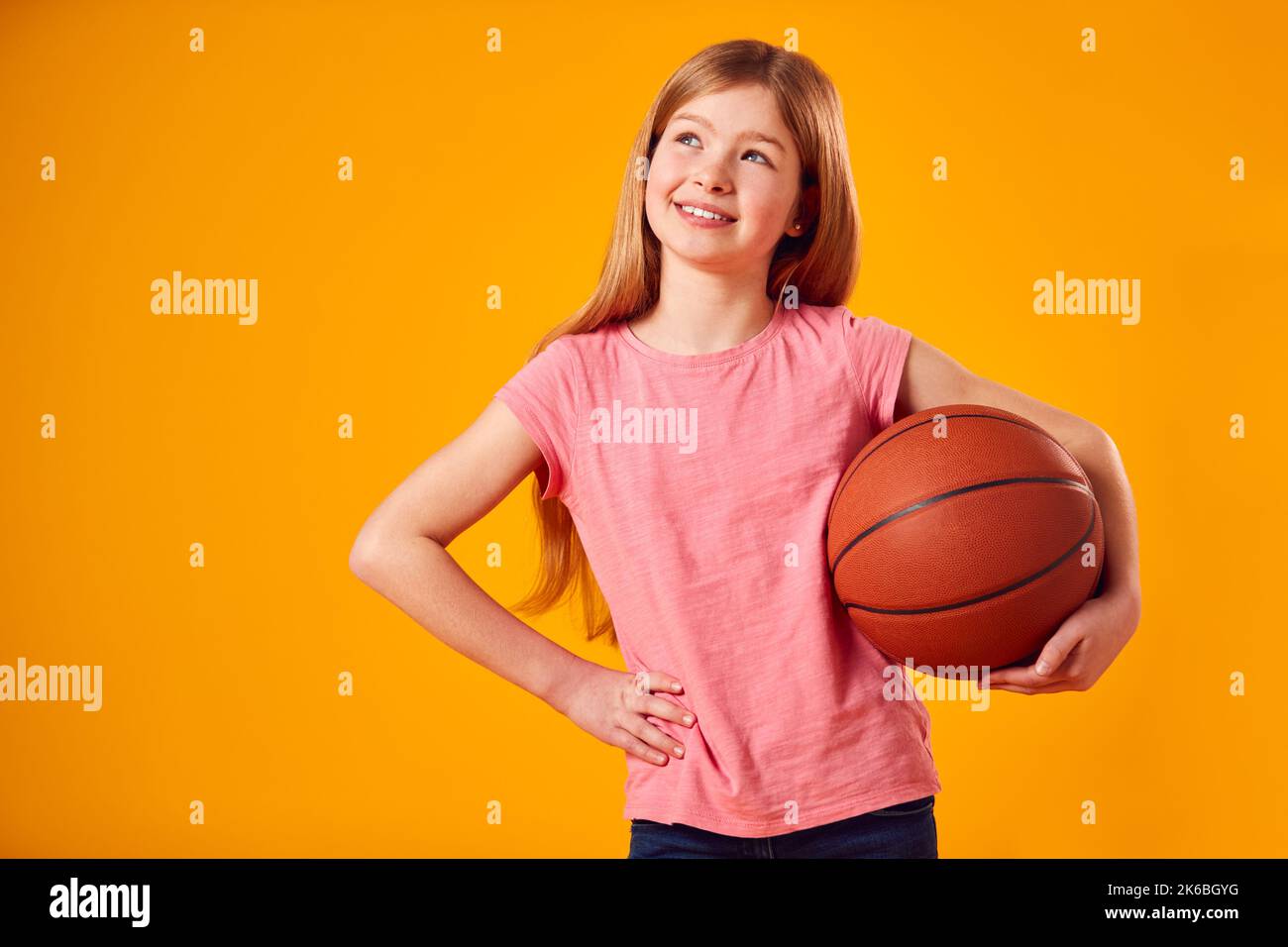 Studio Shot of Young Girl Holding Basketball Under Arm contro sfondo giallo Foto Stock
