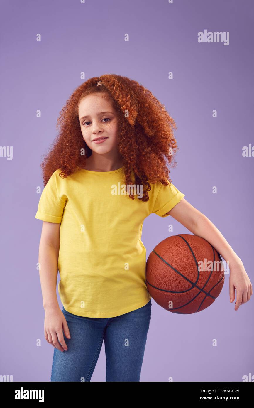 Studio Shot of Young Girl Holding Basketball Under Arm contro sfondo viola Foto Stock
