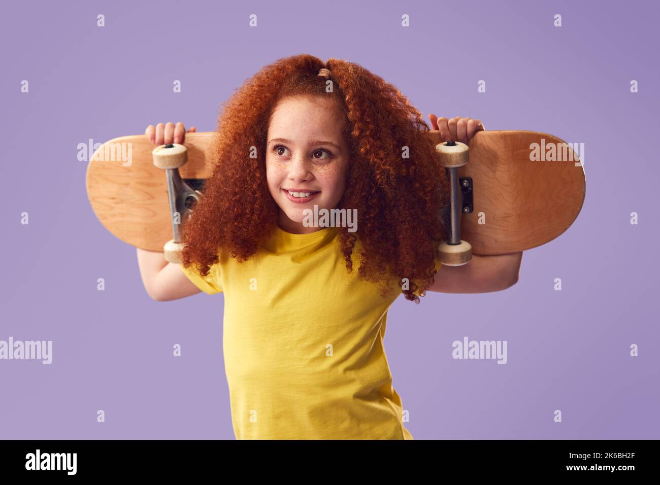 Studio Shot of Young Girl Holding Skateboard sulle spalle contro sfondo viola Foto Stock