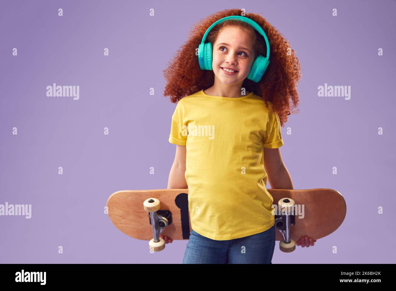 Studio Shot di giovane ragazza indossare cuffie tenendo Skateboard contro sfondo viola Foto Stock