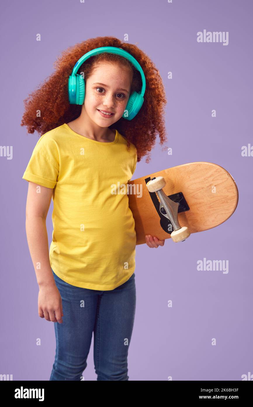 Studio Shot di giovane ragazza indossare cuffie tenendo Skateboard contro sfondo viola Foto Stock