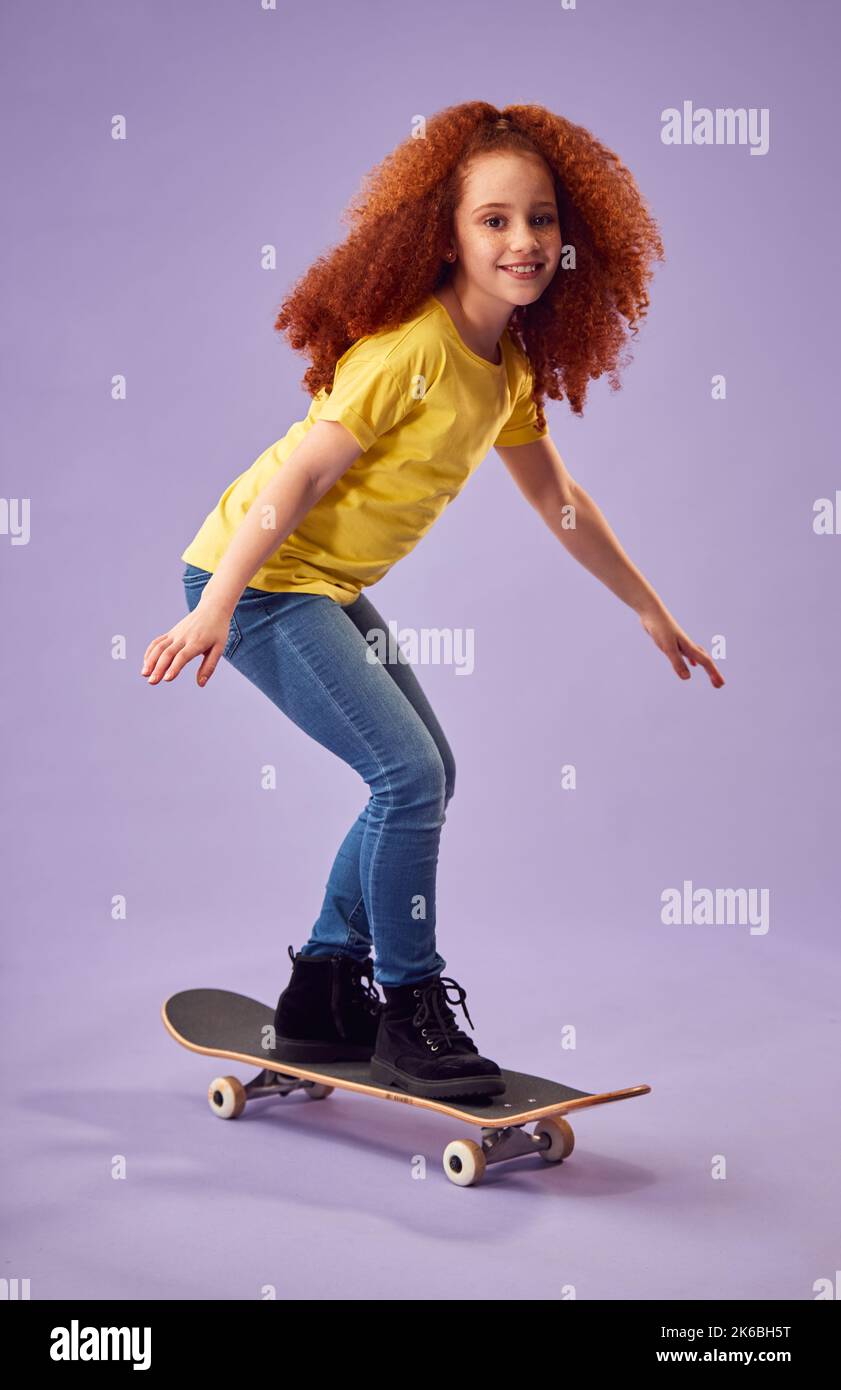 Studio Shot di giovane ragazza Equitazione Skateboard contro sfondo viola Foto Stock