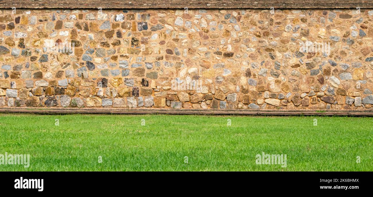 Vista panoramica del vecchio muro di pietra d'epoca e prato verde in un giardino come design paesaggistico Foto Stock
