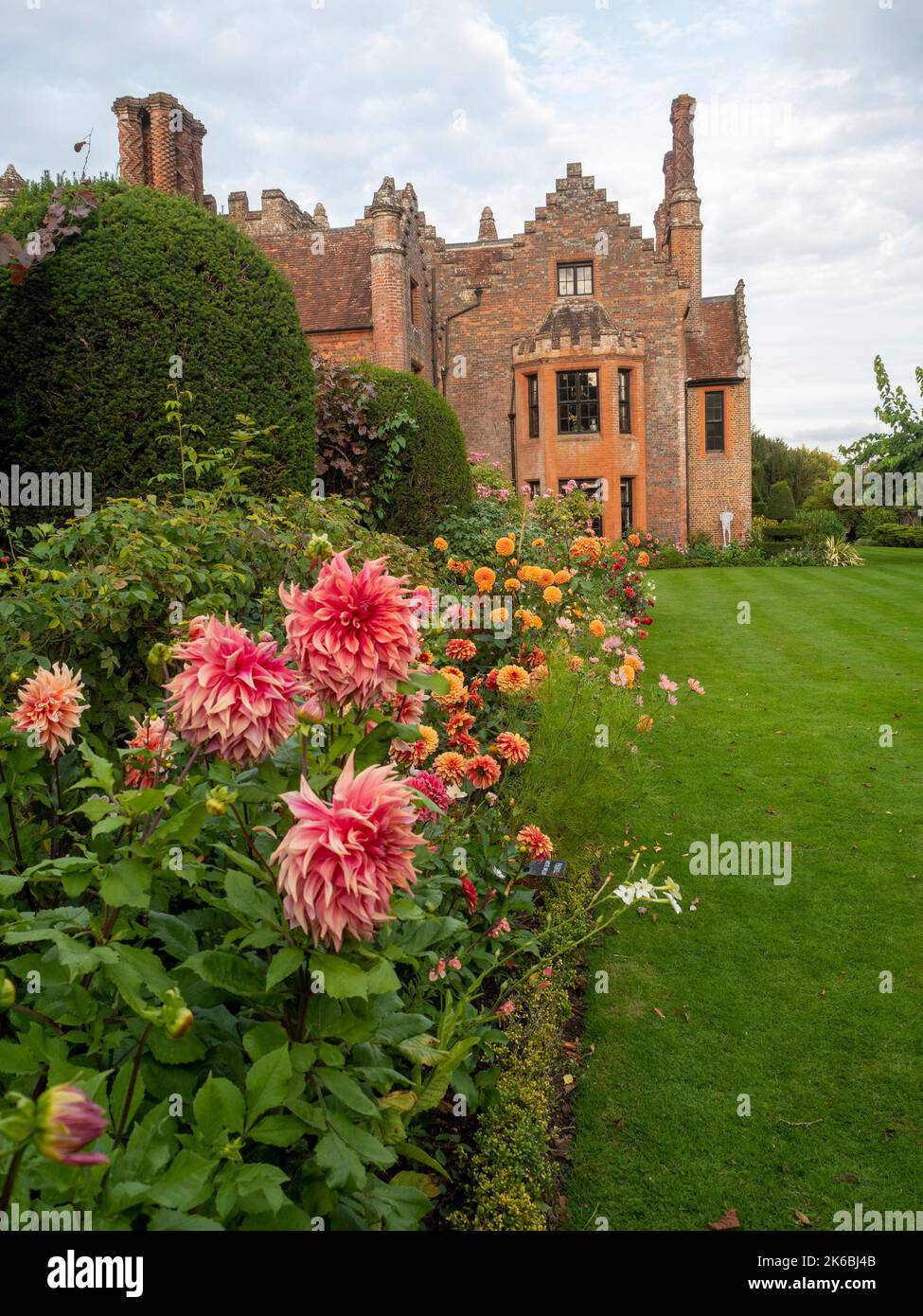 Chenies Manor e giardino circondato da dahlias colorato nel mese di ottobre. Dahlia 'Islander' in primo piano con rosso, arancione in lungo confine erbaceo. Foto Stock