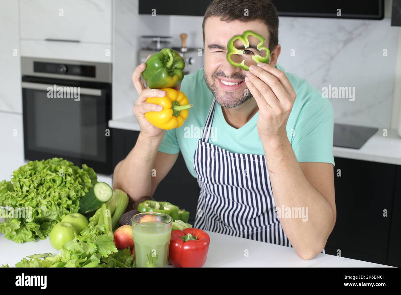 Uomo che gioca con peperoni verdi in cucina Foto Stock