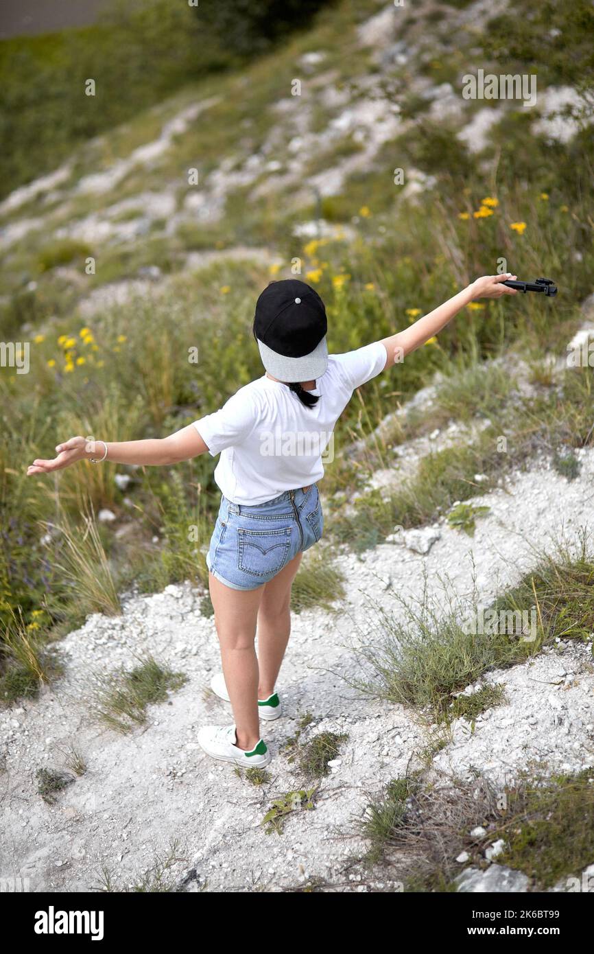 Ragazza in jeans corti con braccia aperte in piedi su una strada rocciosa. Vista dall'alto Foto Stock