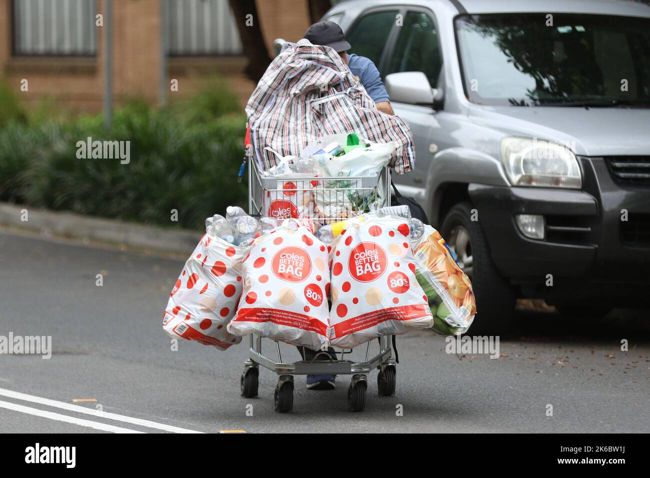 Un uomo spinge un carrello lungo Myrtle Street, Chippendale a Sydney, Australia pieno di sacchetti di lattine e bottiglie che ha raccolto per reclamare il Foto Stock