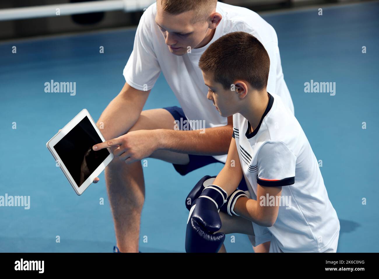 Utilizzo di gadget e tecnologia moderni allo studio. Allenatore sportivo personale che spiega l'asticciola al bambino con i guanti di boxe utilizzando un tablet Foto Stock