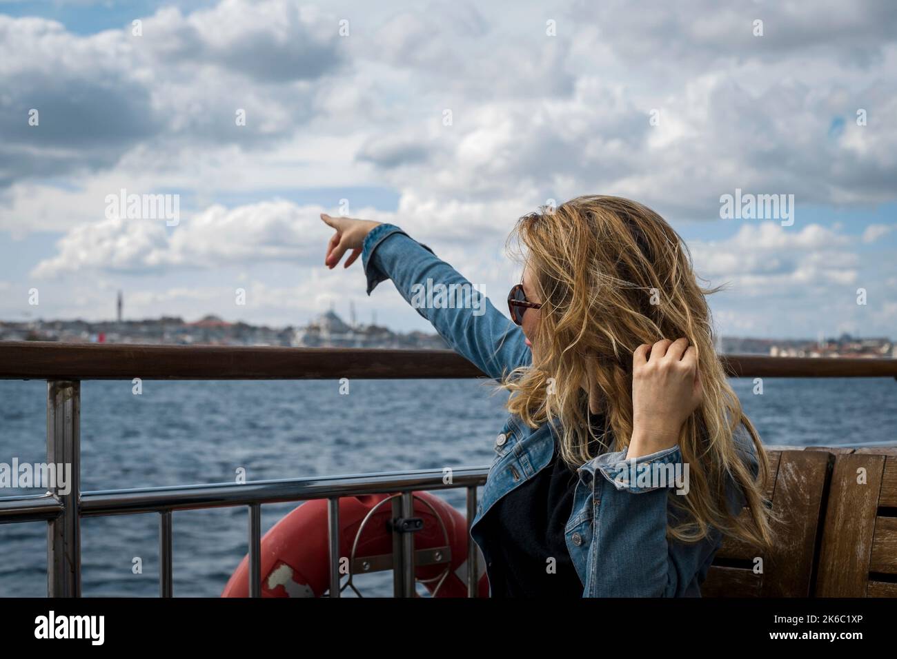 Donna bionda dai capelli lunghi che viaggia in traghetto nel Bosforo, indicando un punto con la mano. Foto Stock