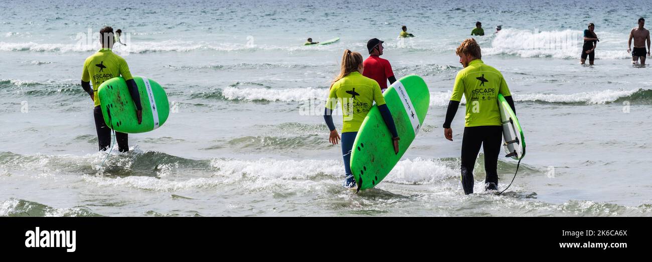 Un'immagine panoramica dei vacanzieri che prendono parte a una lezione di surf con un istruttore a Fistral Beach a Newquay in Cornovaglia nel Regno Unito. Foto Stock