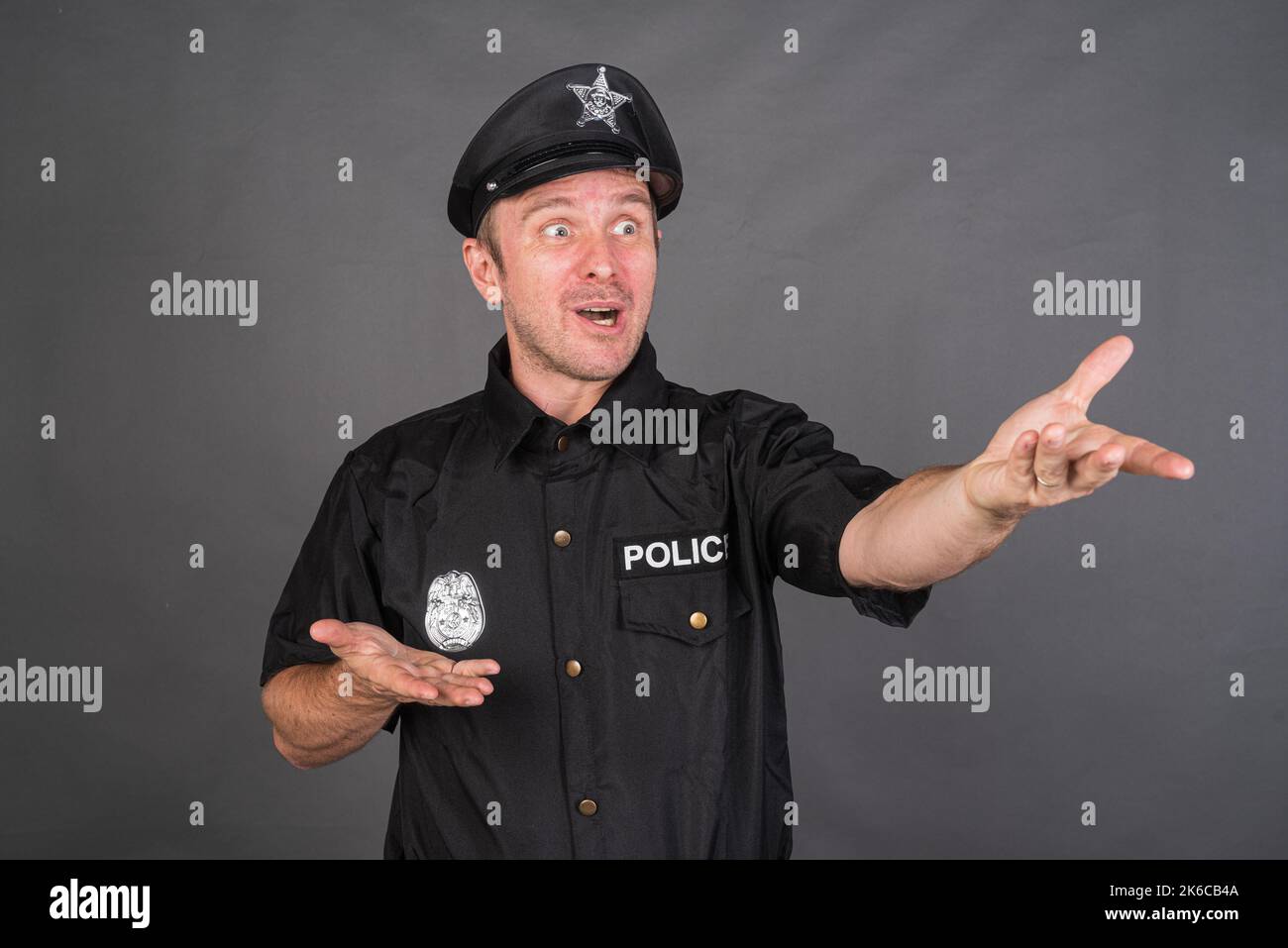 Frustrato uomo caucasico che indossa costume uniforme di polizia contro sfondo grigio studio Foto Stock