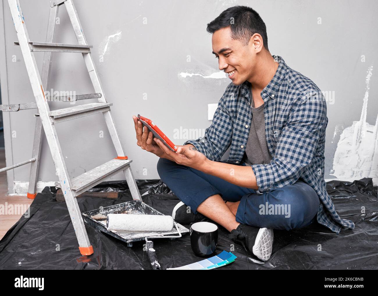 Un giovane uomo asiatico guarda le idee video fai da te e le guide pratiche mentre rinnova Foto Stock