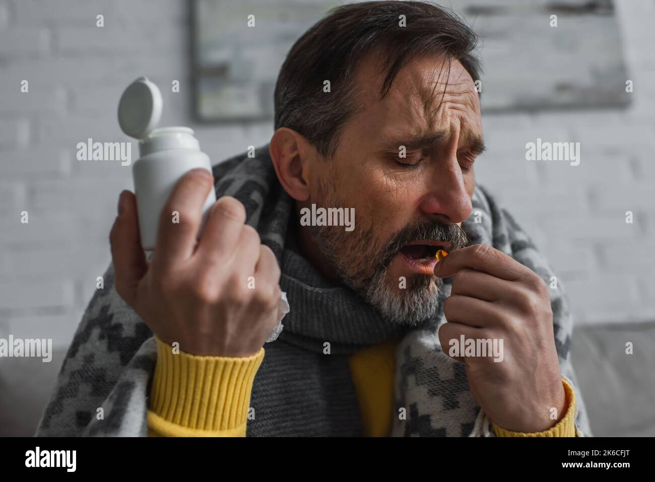 uomo malato con gli occhi chiusi tenendo contenitore e prendendo la pillola a casa, immagine stock Foto Stock