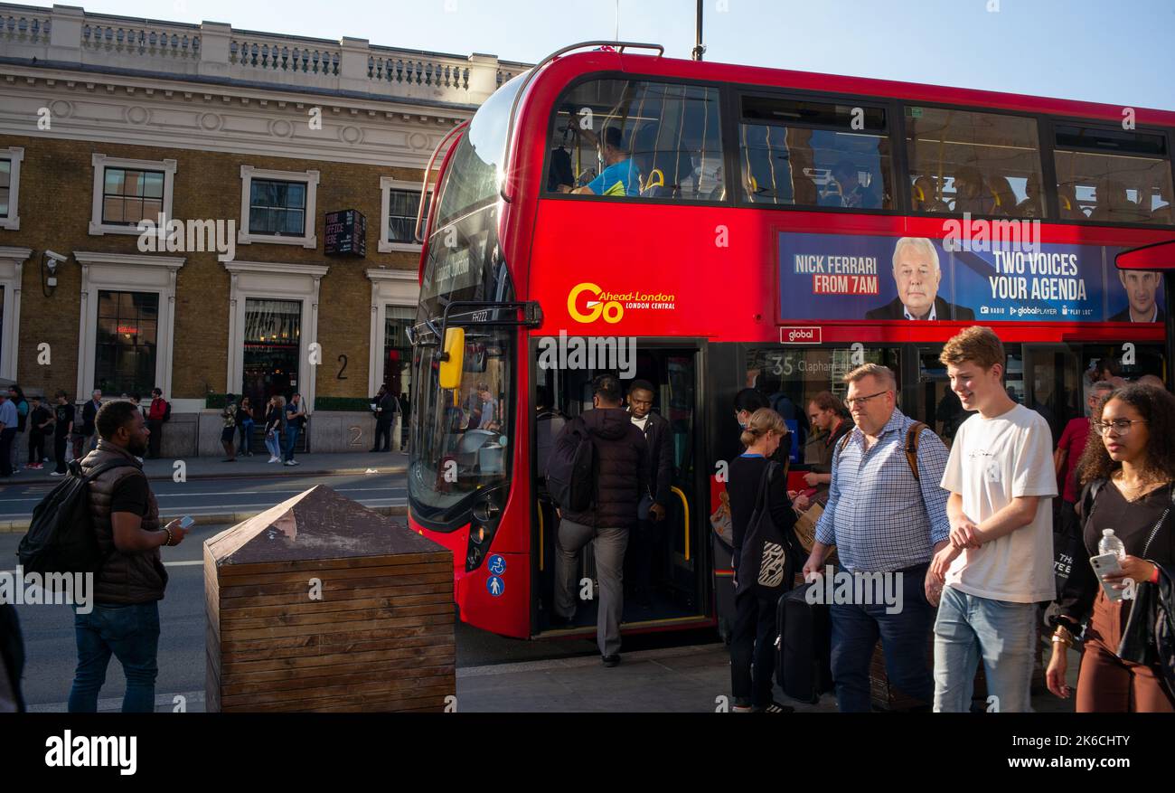 La vita cittadina di Londra catturata in stile fotografico di strada. I passeggeri si alzano dall'autobus rosso quando passano i pendolari, presi al sole della sera. Foto Stock