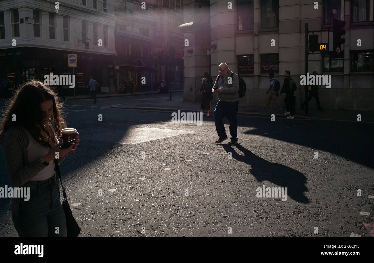 I membri del pubblico distratti dai loro telefoni cellulari perché attraversare la strada a Londra alla luce della sera. Foto Stock