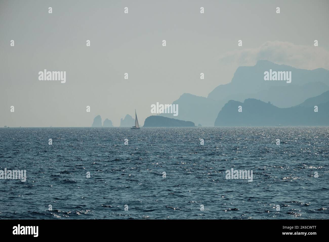 Un singolo yacht passa per l'isola di Capri Italia mentre il sole tramonta in una serata tranquilla in un tranquillo colpo di nebbia. Foto Stock