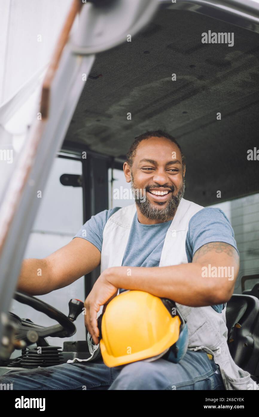 Lavoratore di costruzione felice con l'elmetto seduto nel veicolo Foto Stock