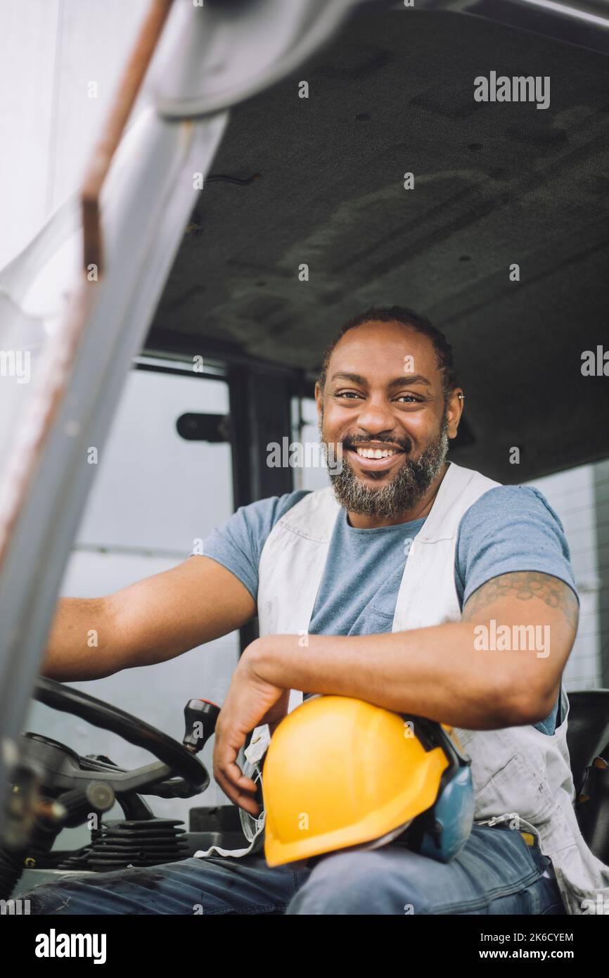 Ritratto di felice lavoratore di costruzione maturo con elmetto seduto nel veicolo Foto Stock