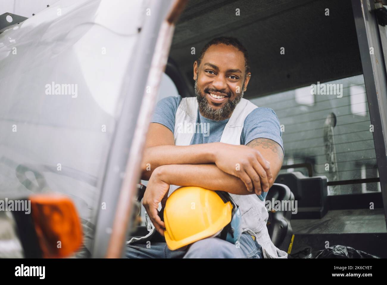 Ritratto di sorridente lavoratore di costruzione maturo con elmetto seduto nel veicolo Foto Stock