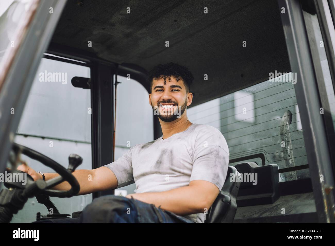 Ritratto di giovane lavoratore felice di costruzione seduto a bordo di un veicolo Foto Stock