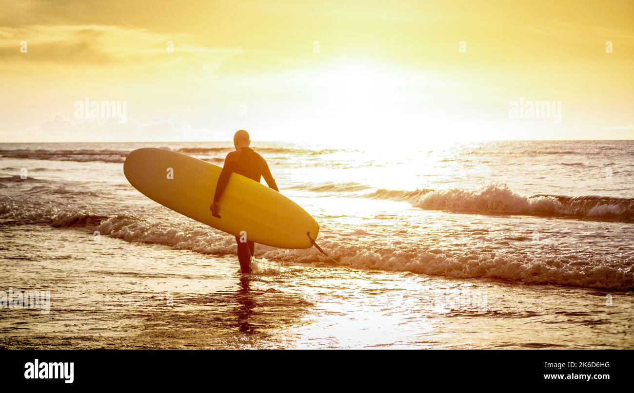 Guy surfer camminando con surf al tramonto a Tenerife - Surf lungo surf formazione professionista in azione - Sport concetto di viaggio con acqua di fuoco Foto Stock