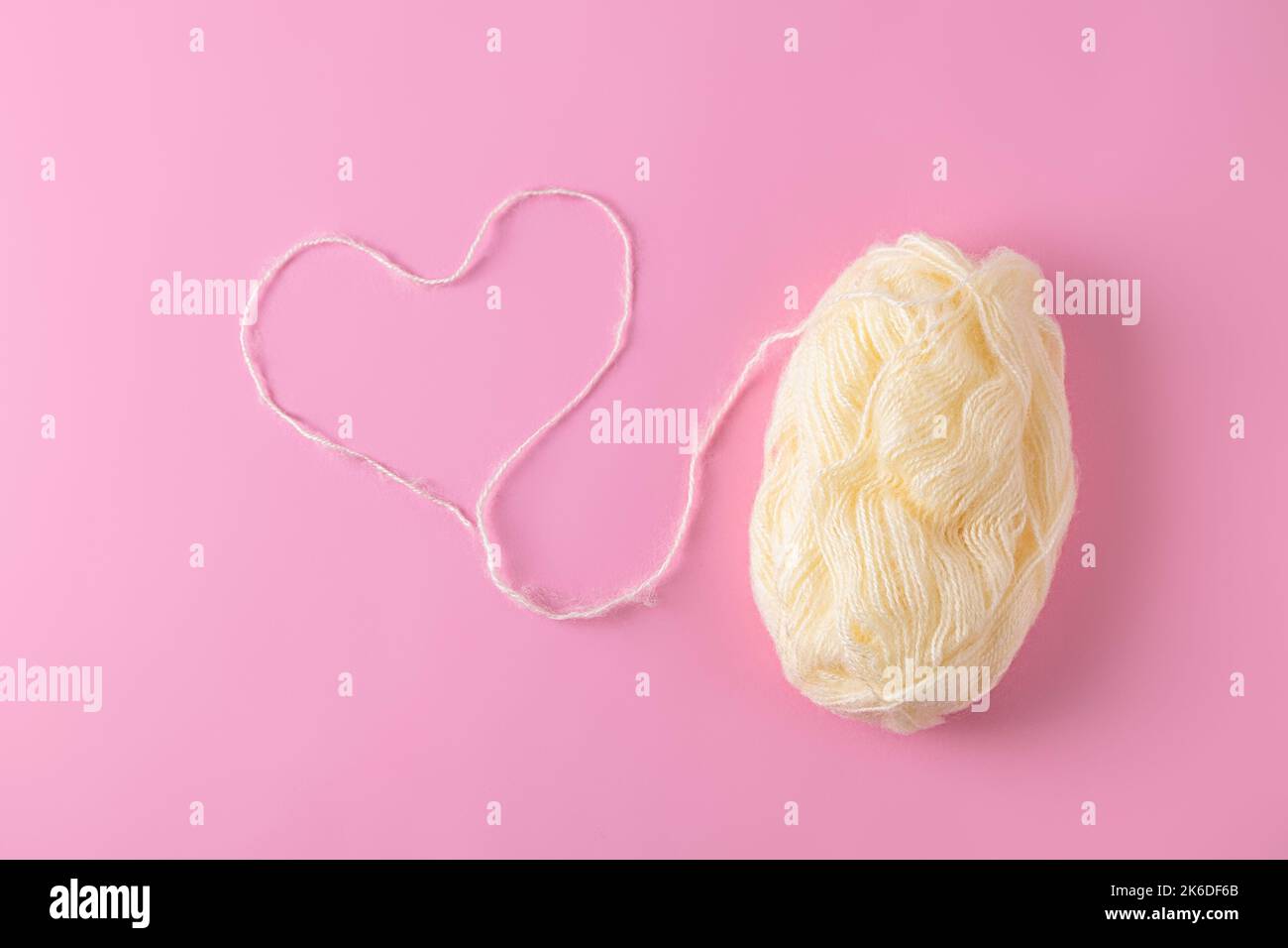Vista dall'alto del cuore in filo di lana con palla di filato su sfondo rosa chiaro Foto Stock