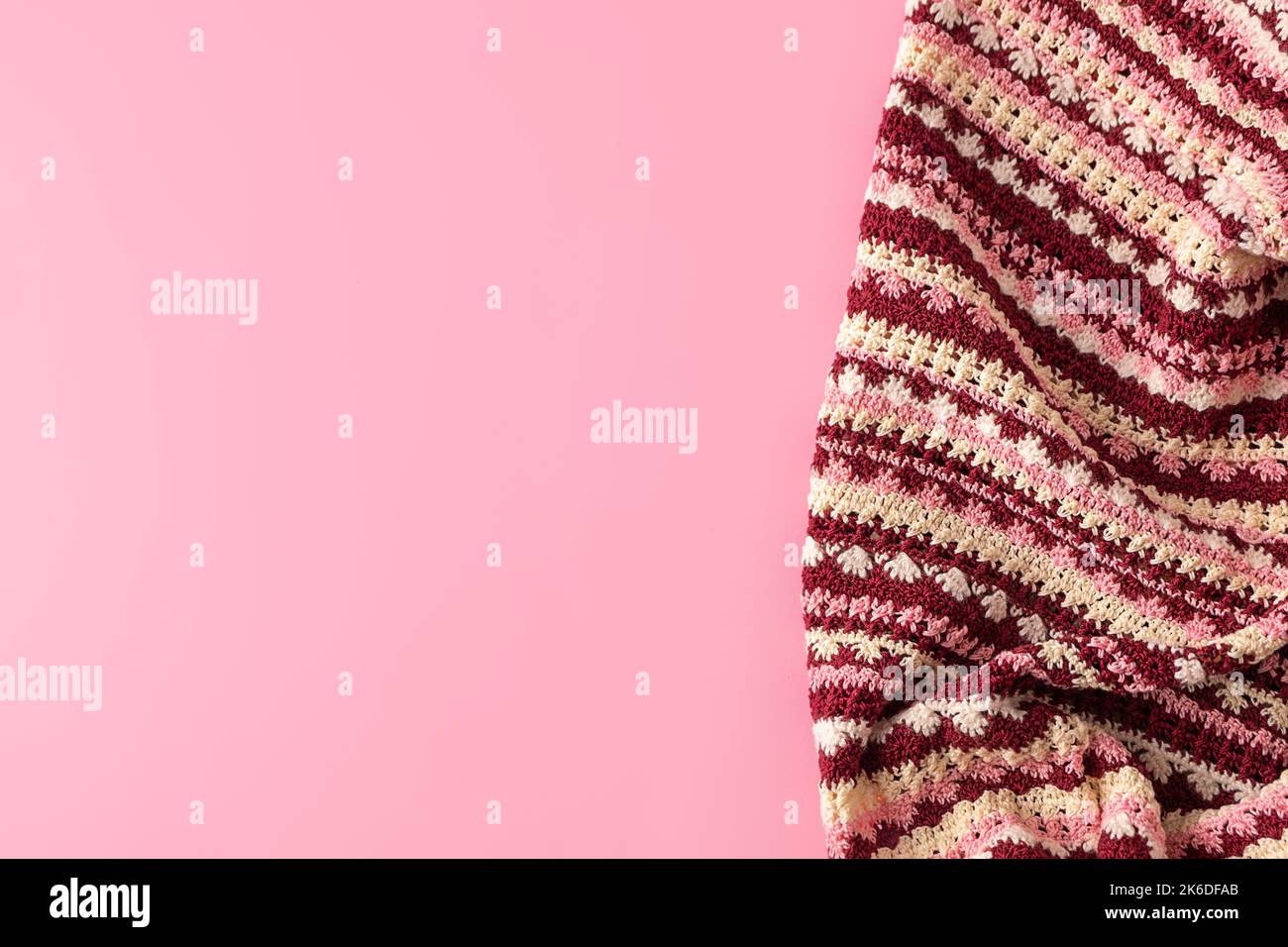 Vista dall'alto della colorata coperta a crochet fatta a mano su sfondo rosa pastello con spazio copia, mockup Foto Stock