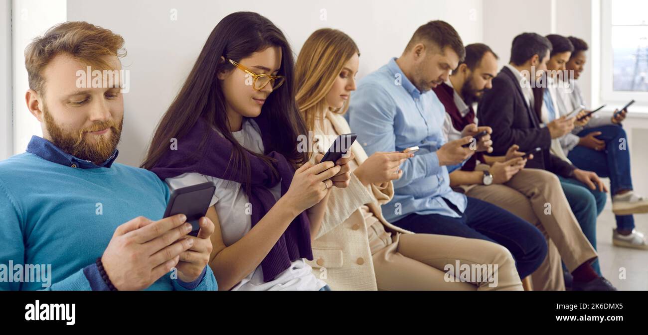 Gruppo di giovani uomini e donne seduti in ufficio e messaggi di testo sui loro telefoni cellulari Foto Stock