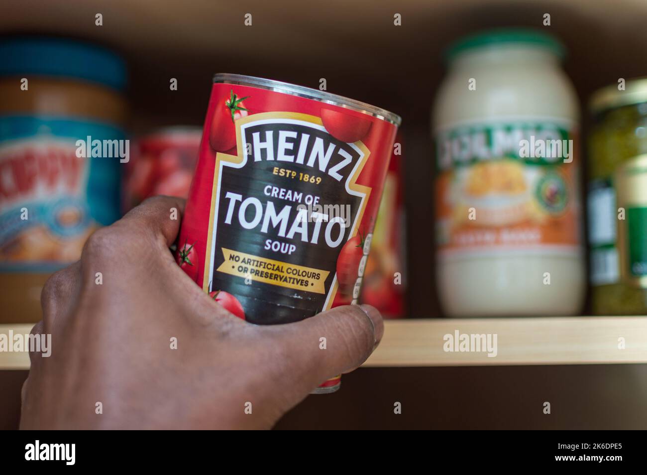 Uomo adulto che prende una lattina di zuppa di pomodoro Heinz dal credenza Foto Stock