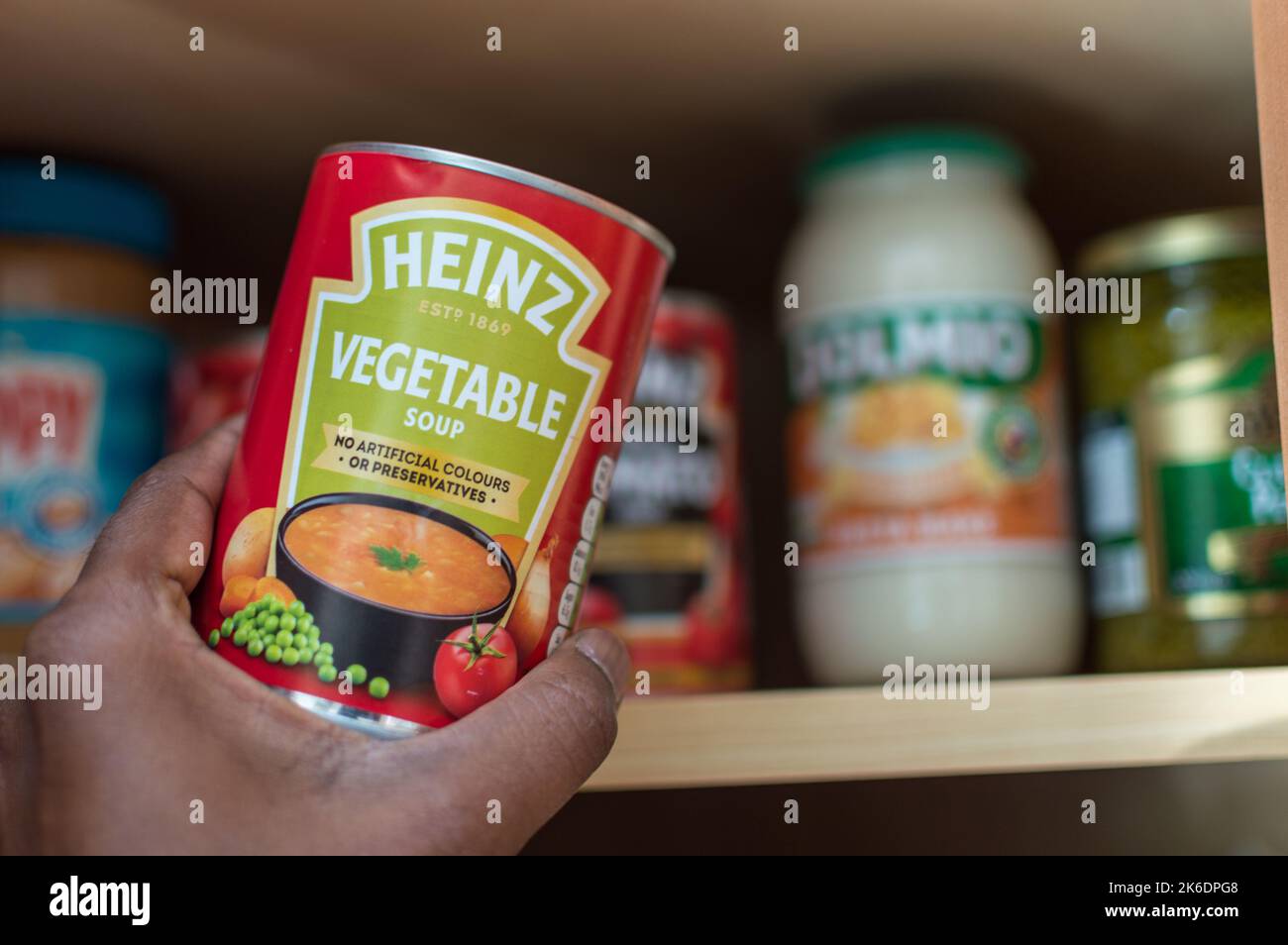 Maschio adulto che prende una lattina di minestra di verdure di Heinz dall'armadietto Foto Stock