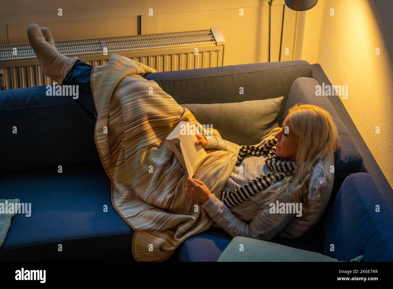 Immagine simbolica risparmio energetico, freddo inverno, crisi energetica, freddo piatto, madre e figlia sdraiata, vestita calorosamente sul divano, lume di candela, riscaldamento su un Foto Stock