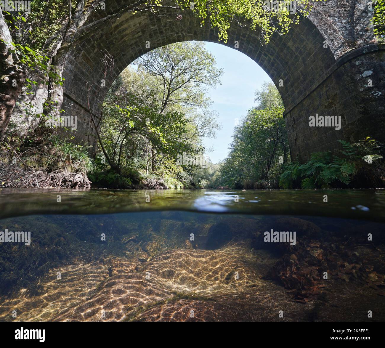 Fiume sotto l'arco di un ponte di pietra, vista su e sotto la superficie dell'acqua, Spagna, Galizia, fiume Oitaven, provincia di Pontevedra Foto Stock