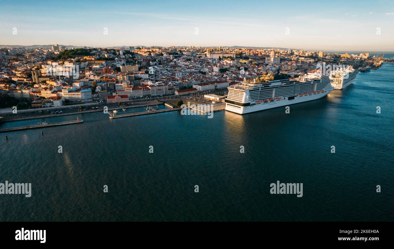 Vista aerea da drone di una grande nave da crociera ormeggiata al porto di Lisbona, Portogallo, con i punti di riferimento di Lisbona sullo sfondo Foto Stock