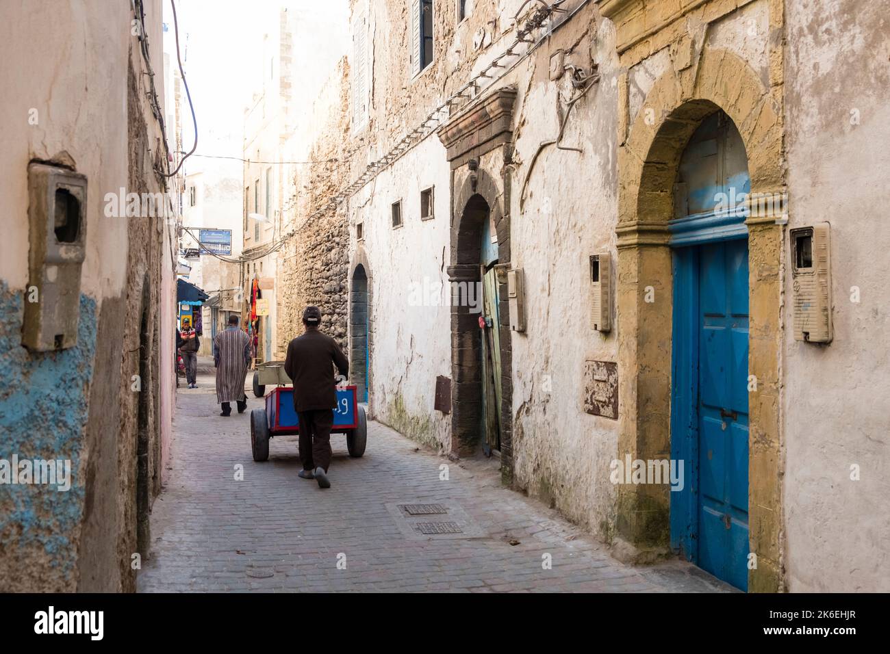 L'uomo spinge il carrello di consegna attraverso una strada stretta nella storica medina della città vecchia di Essaouira, Marocco, Nord Africa Foto Stock