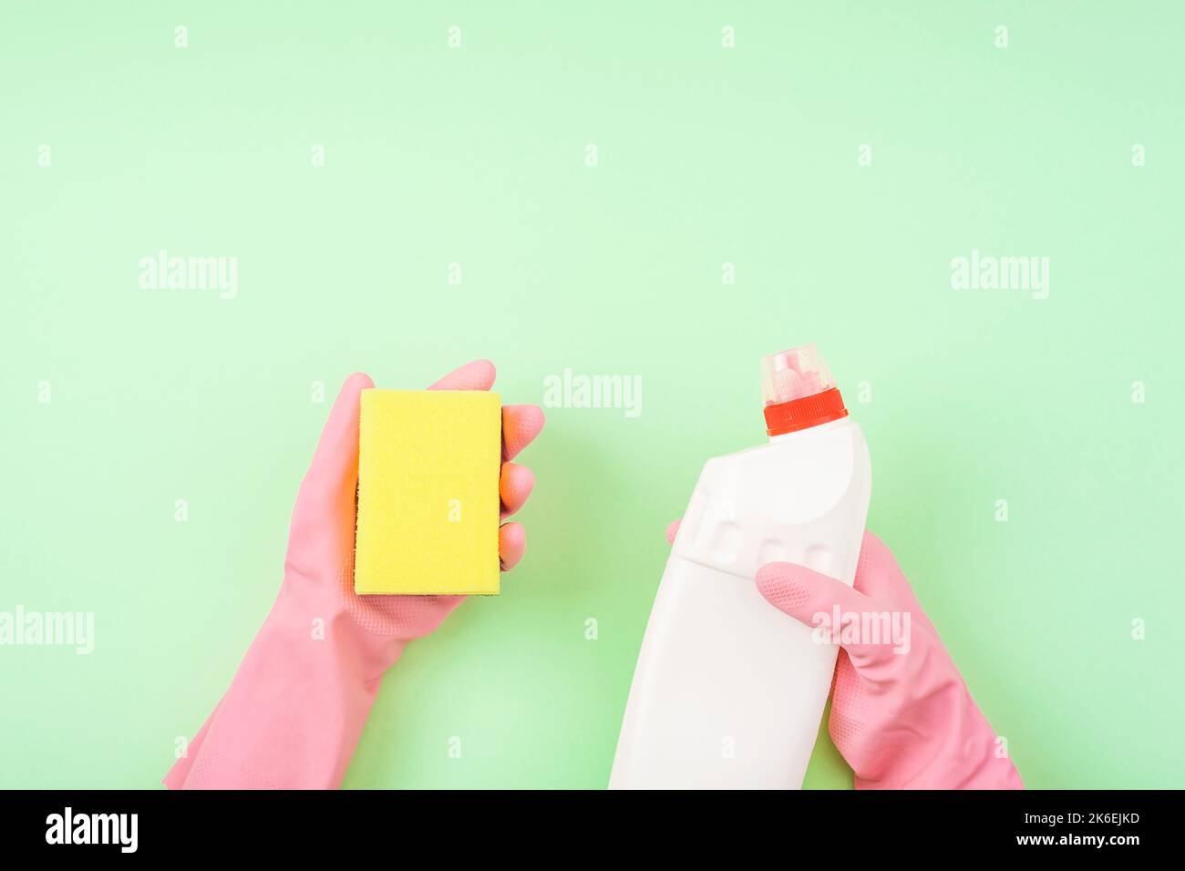 Mano del pulitore in gomma rosa flacone di protezione con detergente e spugna gialla su fondo verde. Vista dall'alto. Foto Stock