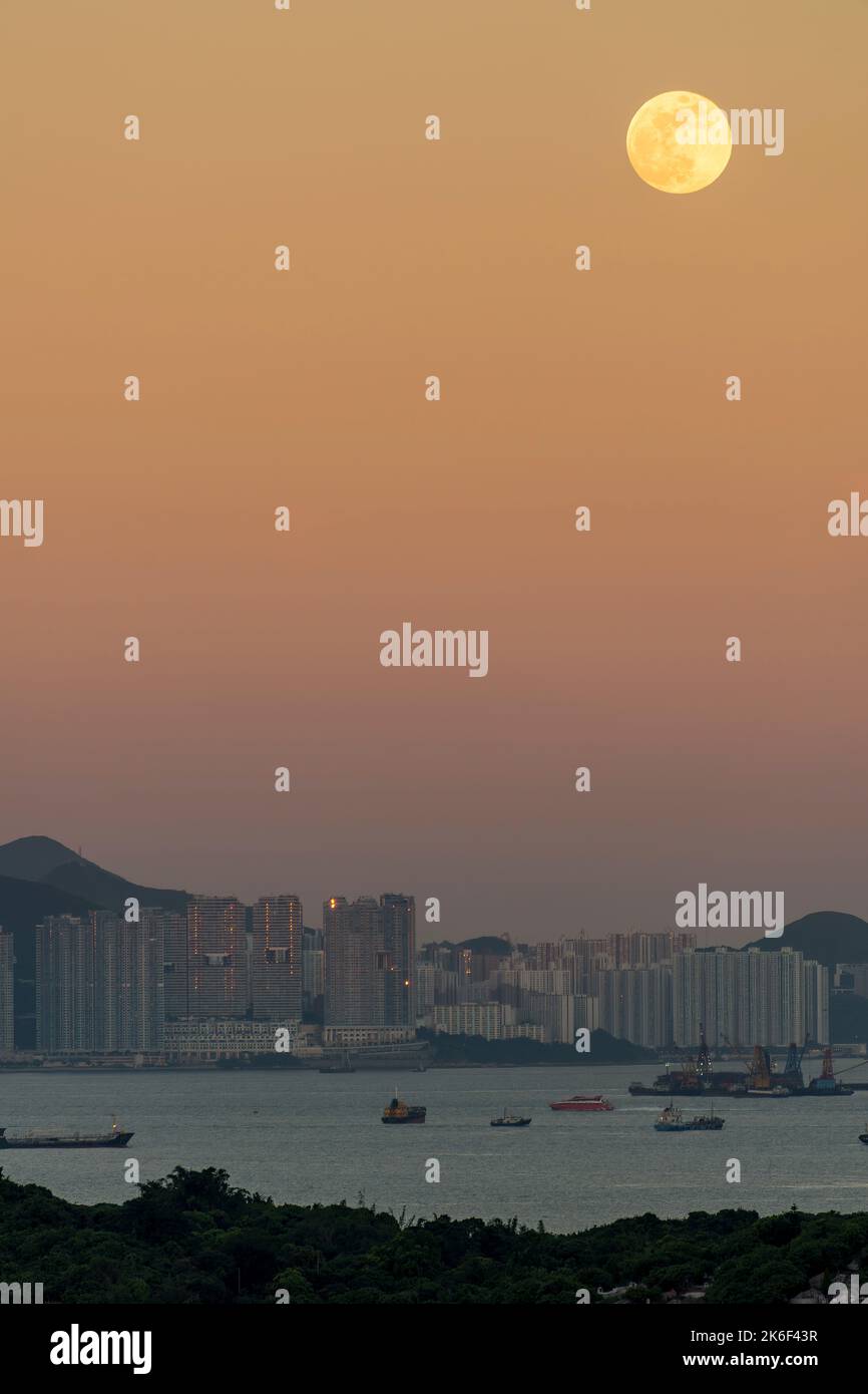 La luna piena sorge attraverso il cielo arancione orientale, con il sole che tramonta negli alti edifici di Pol fu Lam, Isola di Hong Kong Foto Stock