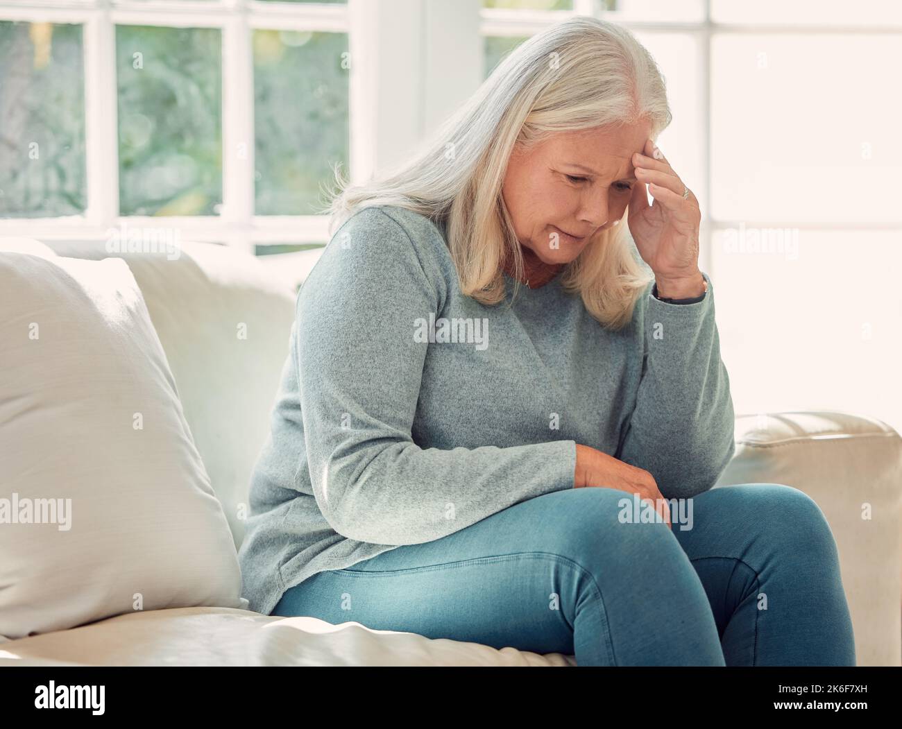 È giusto imparare da ogni esperienza. una donna anziana che ha un mal di testa sul divano a casa. Foto Stock