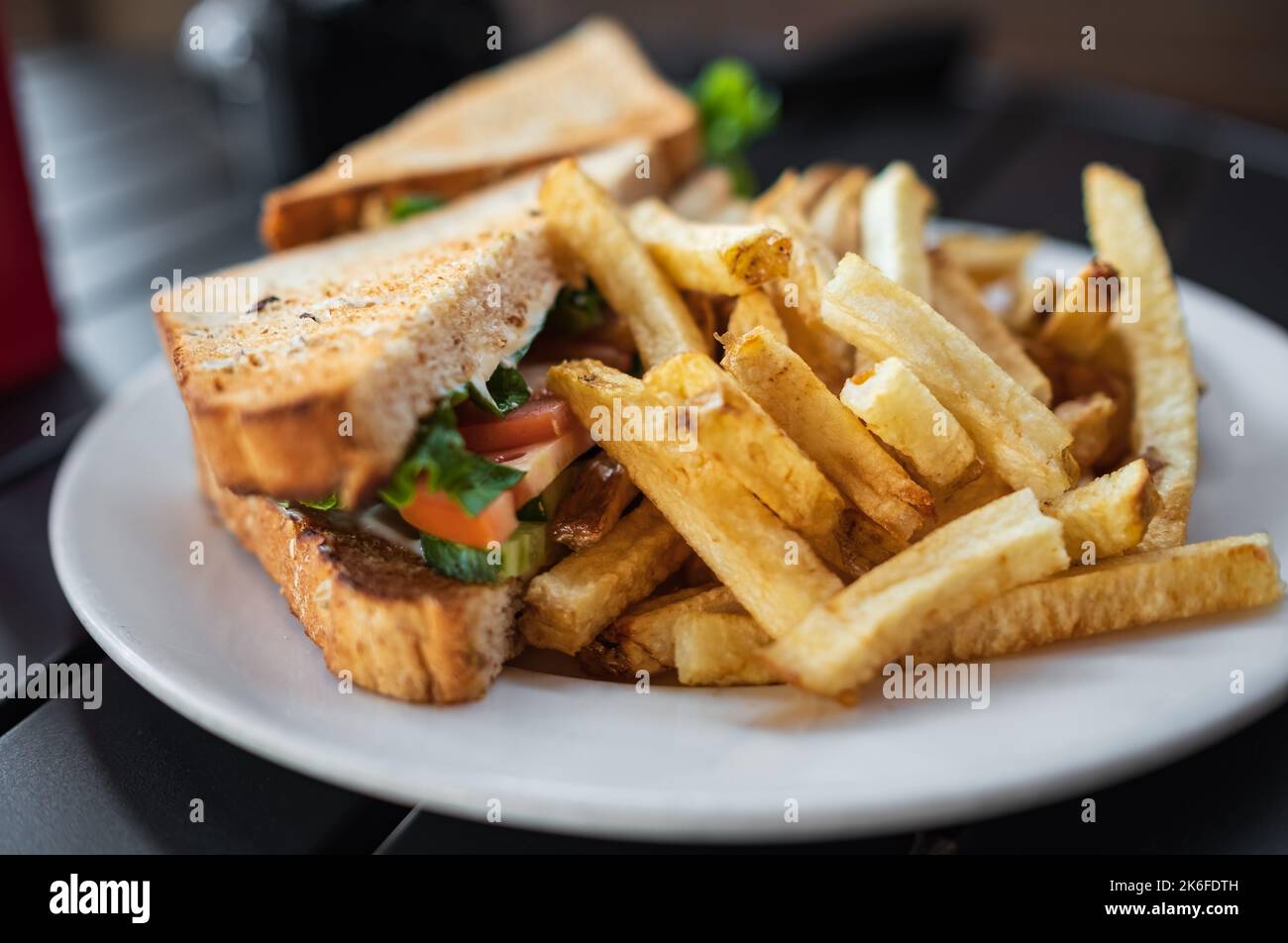 Club-sandwich con patatine fritte su piatto bianco. Sandwich alla griglia con ketchup e patatine salate. Nessuno, sfocato, fuoco selettivo Foto Stock