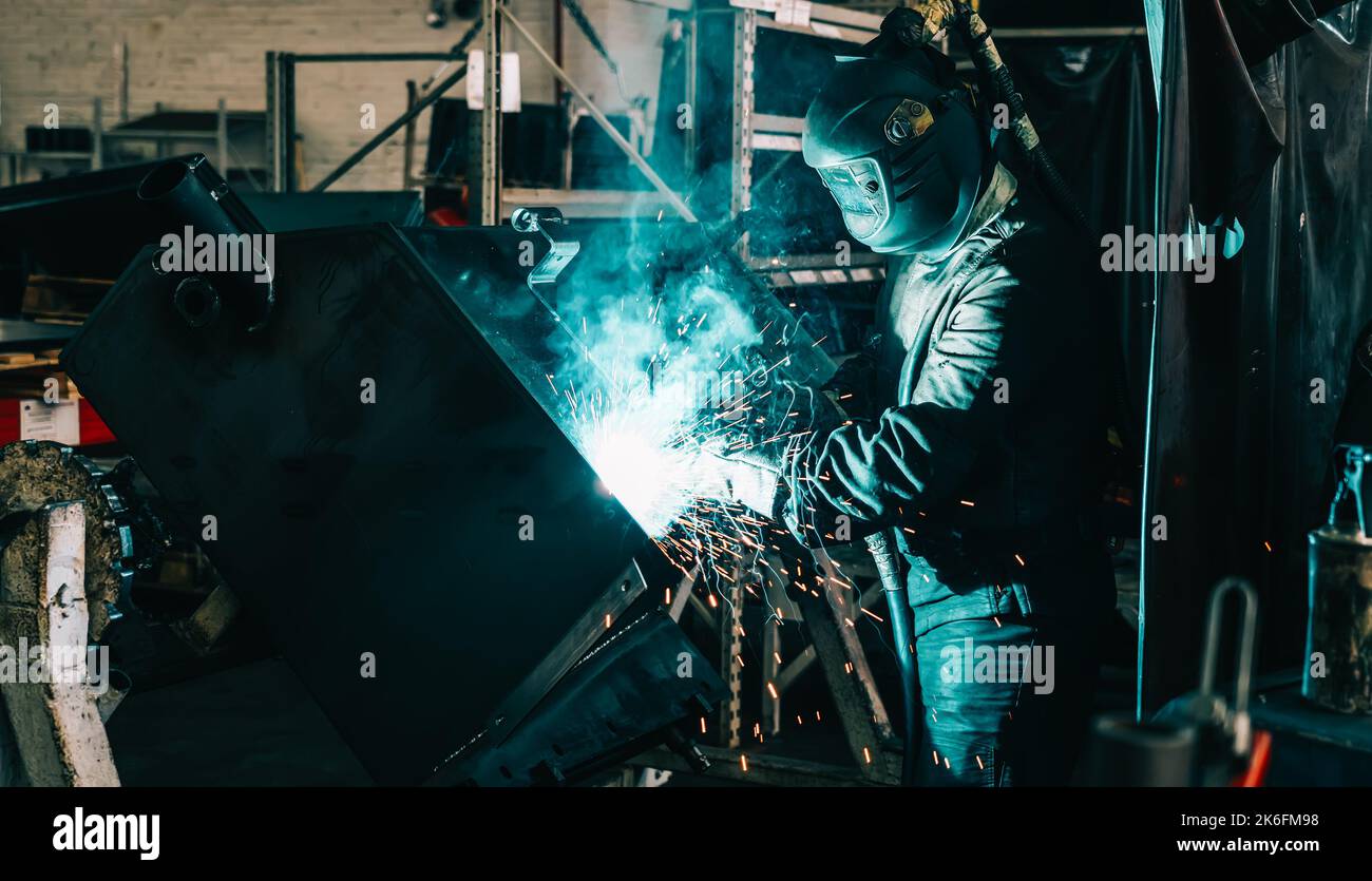 Saldatrice industriale in acciaio in lavorazione in fabbrica di metallo. Scintille e fumo volano dalla saldatura. Foto Stock