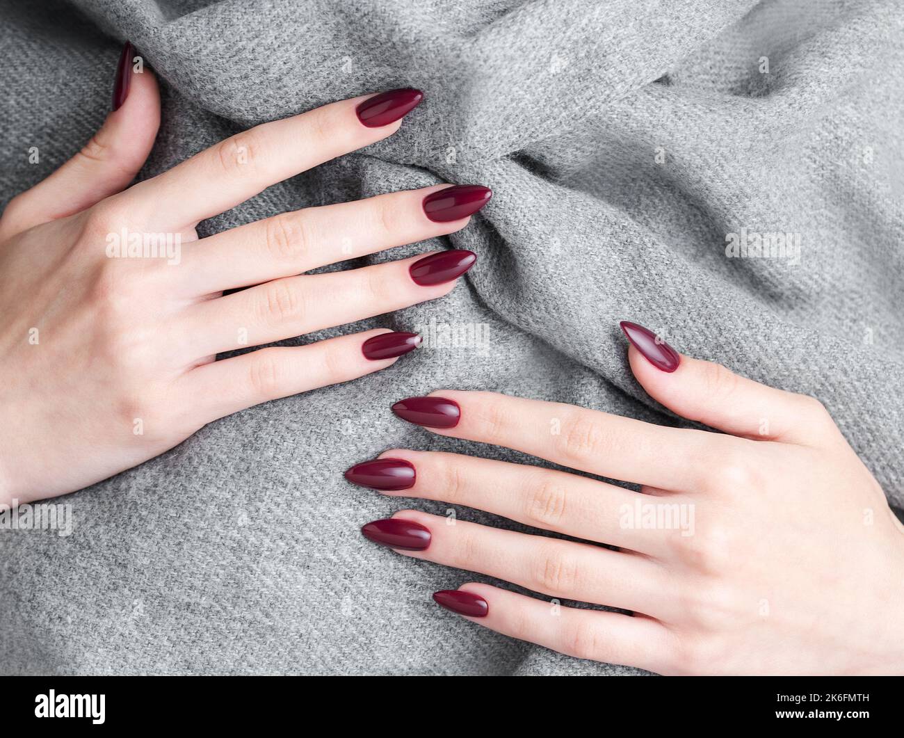 Belle mani di una giovane donna con manicure rosso scuro sulle unghie. Autunno inverno progettazione unghie concetto di trattamento di bellezza. Foto Stock