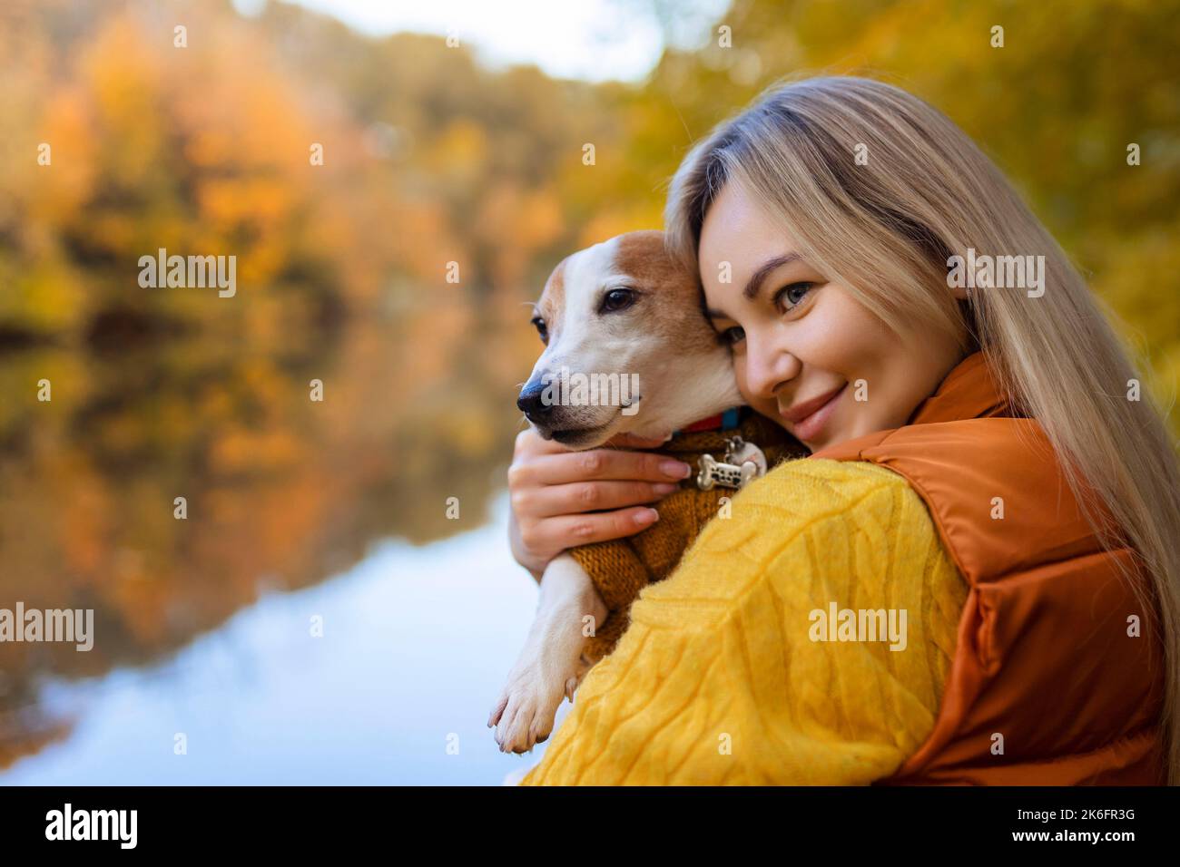 Ritratto di una giovane donna sorridente che bacia un cane in un campo. Ragazza elegante amante del cane che abbraccia il suo cane mentre cammina. Concetto di amicizia animale Foto Stock