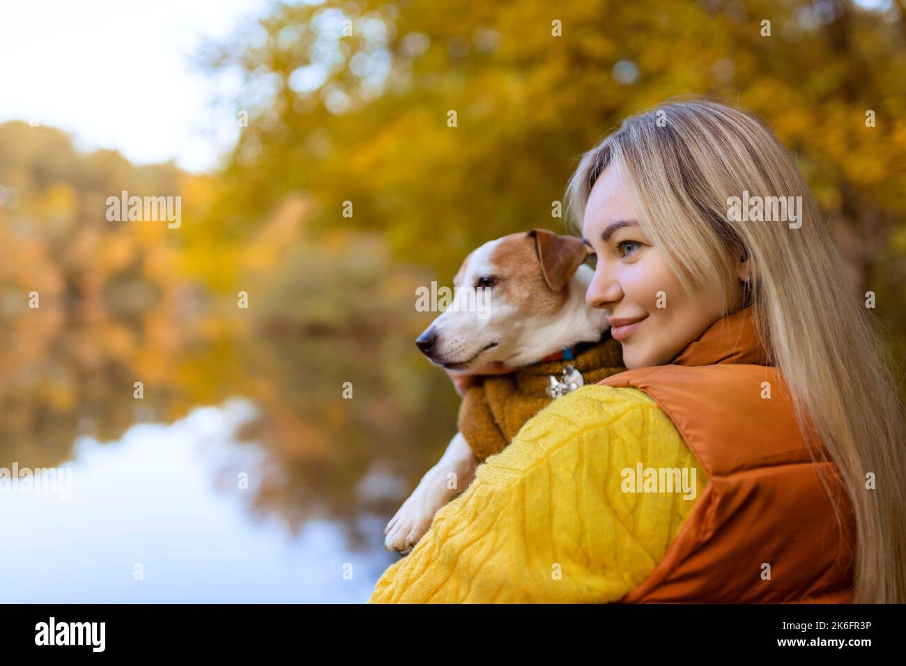 Ritratto di una giovane donna sorridente che bacia un cane in un campo. Ragazza elegante amante del cane che abbraccia il suo cane mentre cammina. Concetto di amicizia animale Foto Stock