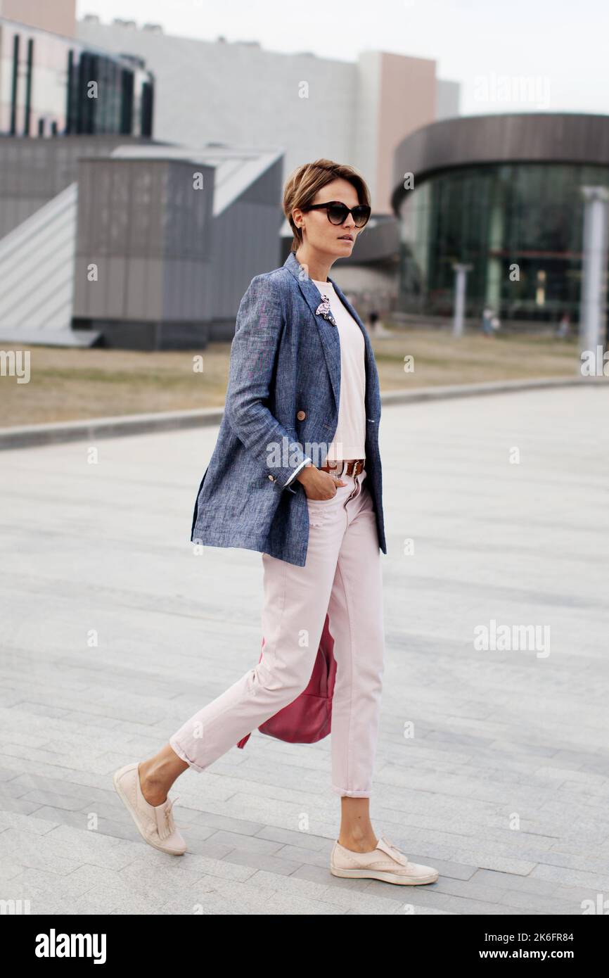 Bella emancipata donna di affari capelli corti con fiducia camminando strada. Determinazione donna alla moda indossa giacca e pantaloni Foto Stock