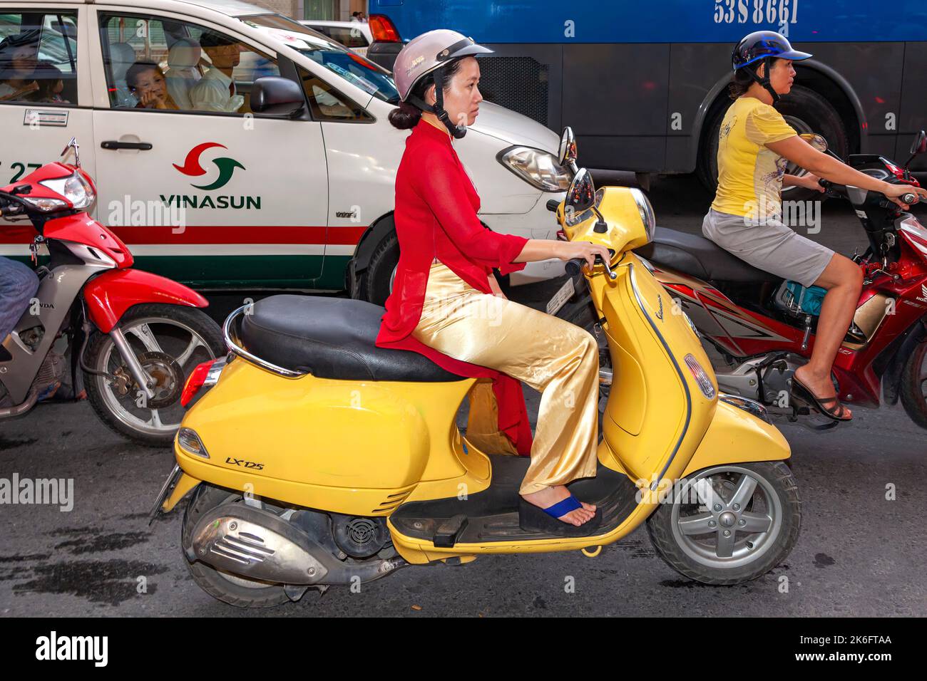Signora vietnamita che indossa ao dai e casco scooter in circolazione, ho Chi Minh City, Vietnam Foto Stock