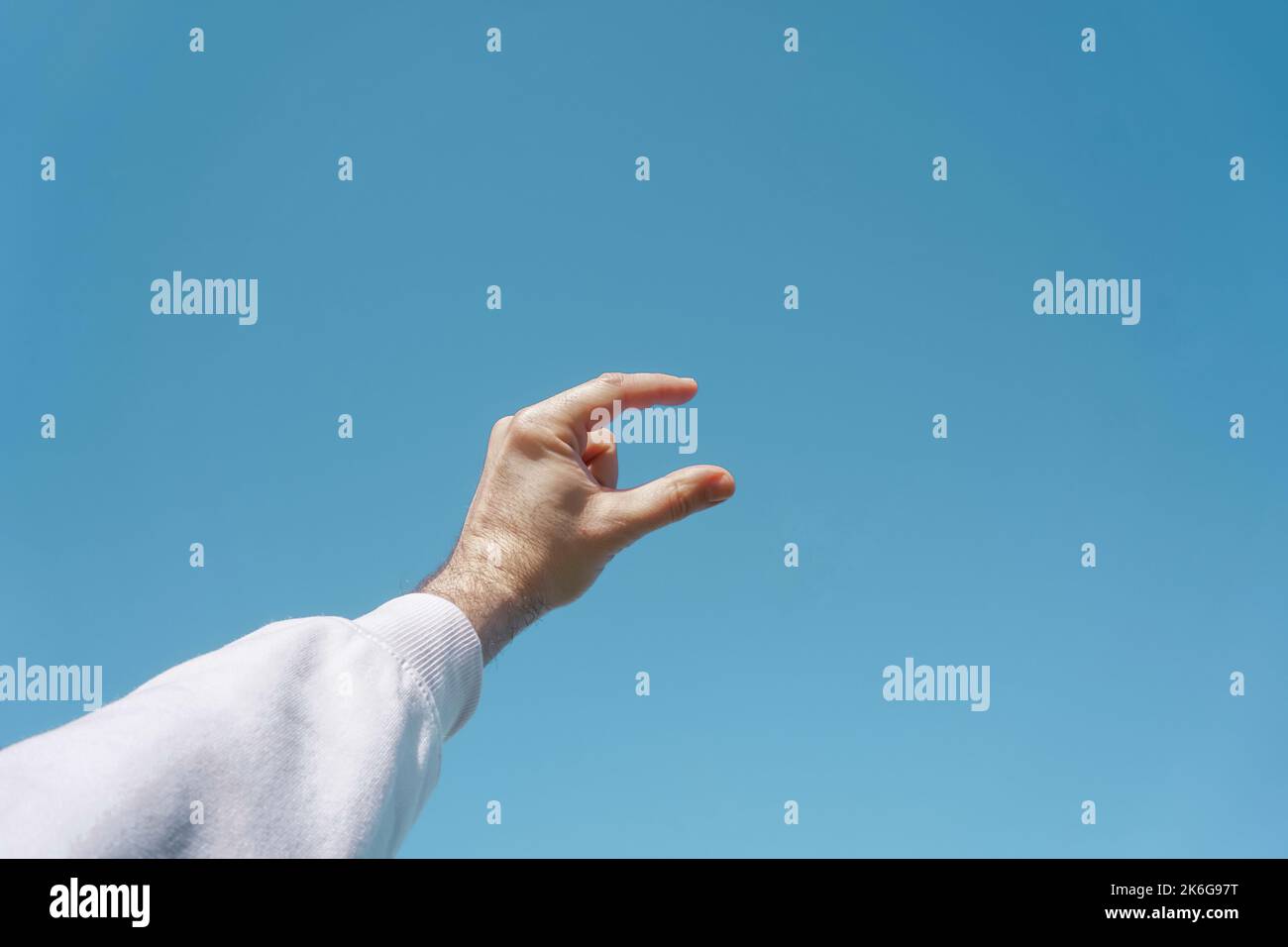 mano in su nell'aria gesturing nel cielo blu, fondo blu Foto Stock
