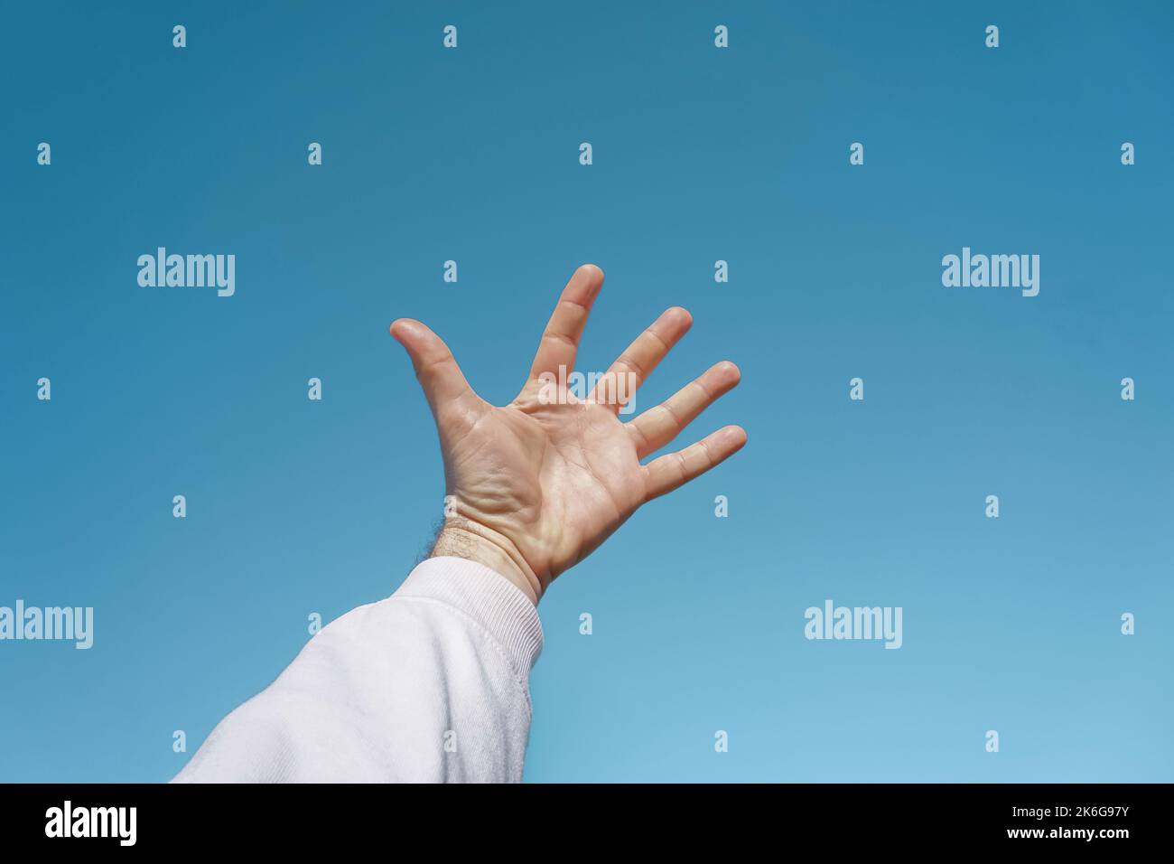 mano in su nell'aria gesturing nel cielo blu, fondo blu Foto Stock