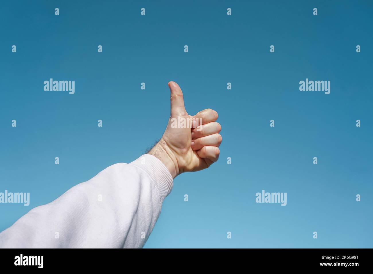 mano in su nell'aria gesturing nel cielo blu, fondo blu Foto Stock