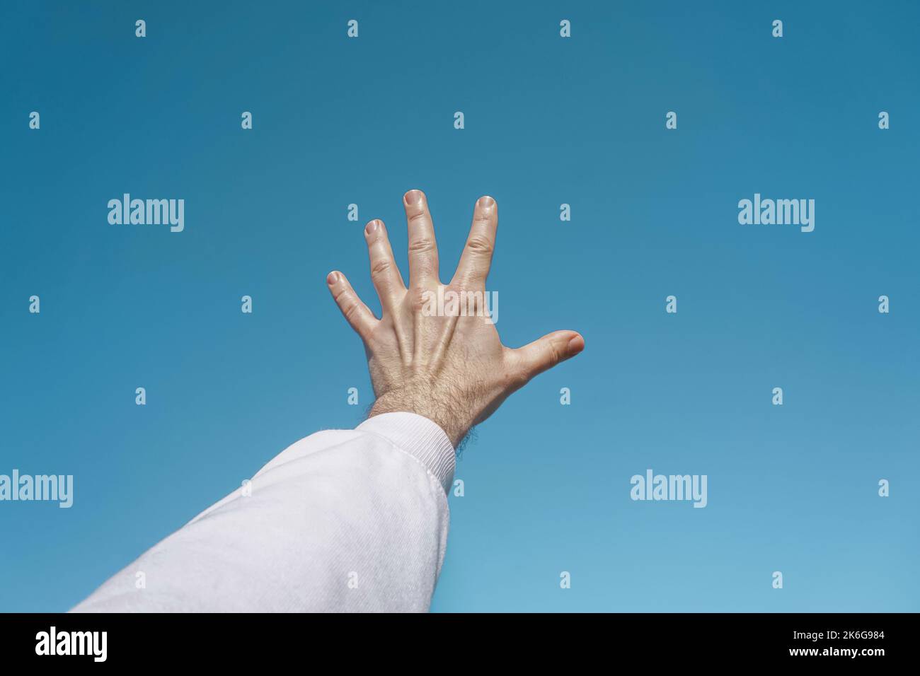 mano in su nell'aria gesturing nel cielo blu, fondo blu Foto Stock